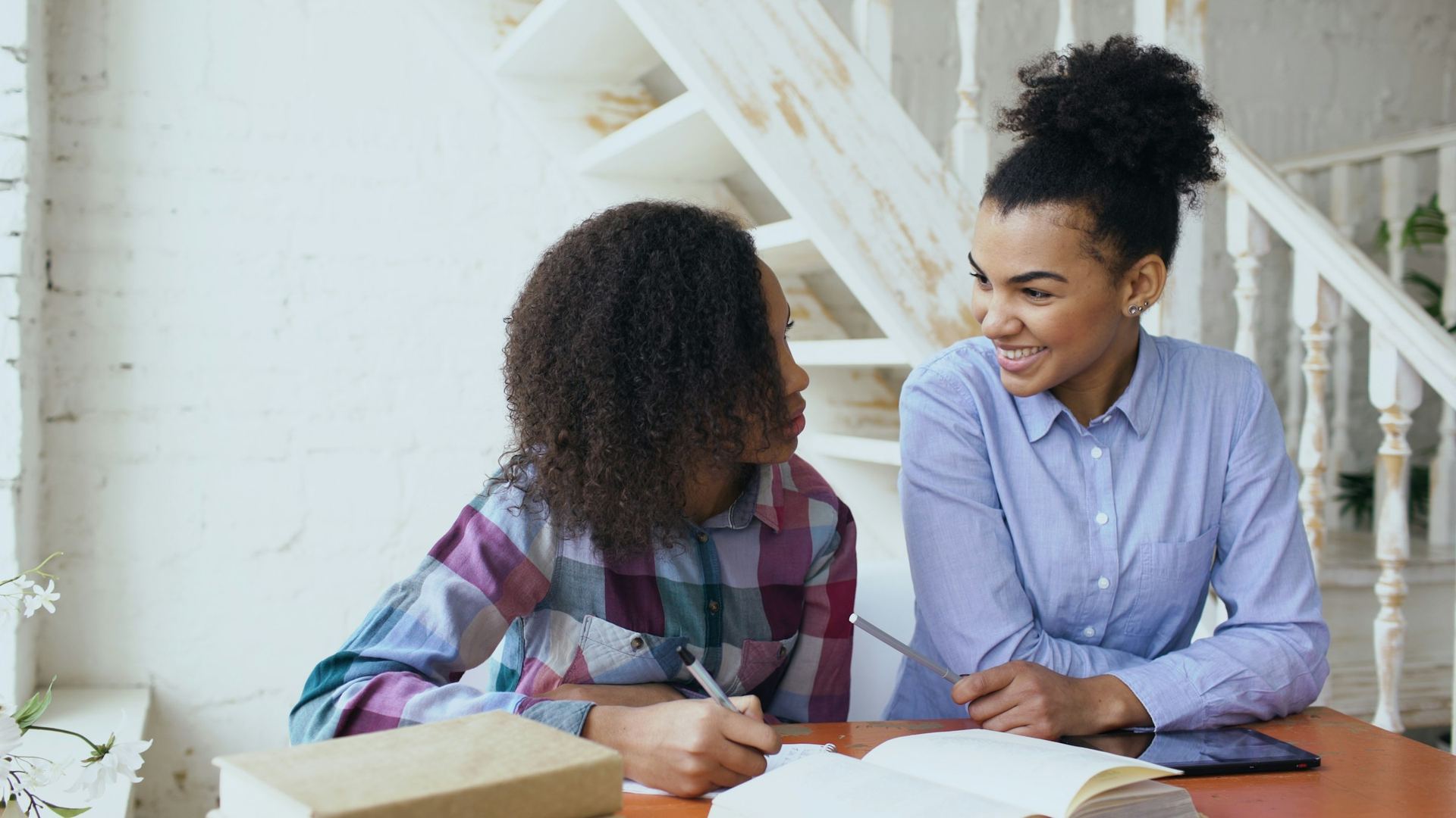 A young volunteer tutor smiles while helping a middle school girl with her schoolwork