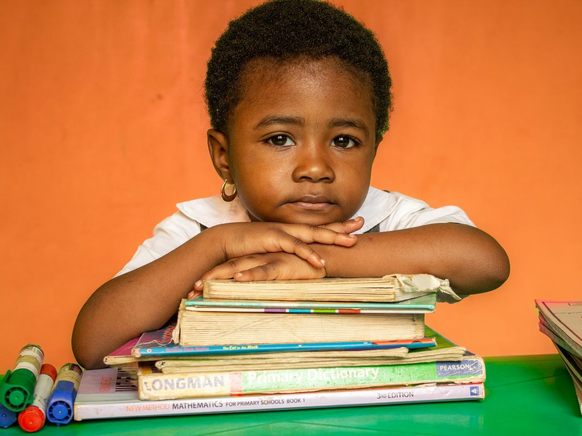 A young boy rests his chin on a stack of schoolbooks