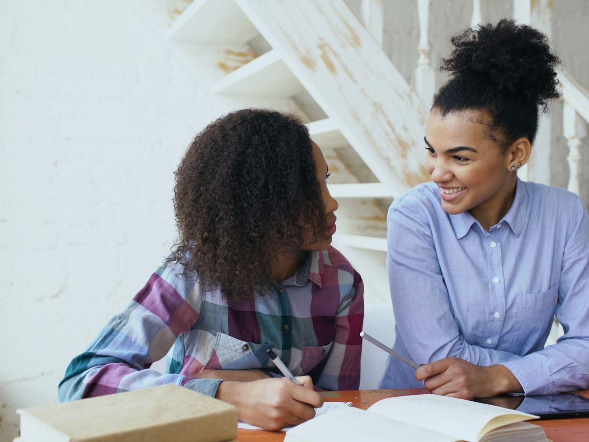 A college-age volunteer reviews schoolwork with a teenage girl